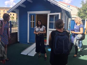 Image is a blue shed with an accessible ramp entrance, with some people standing in front of it